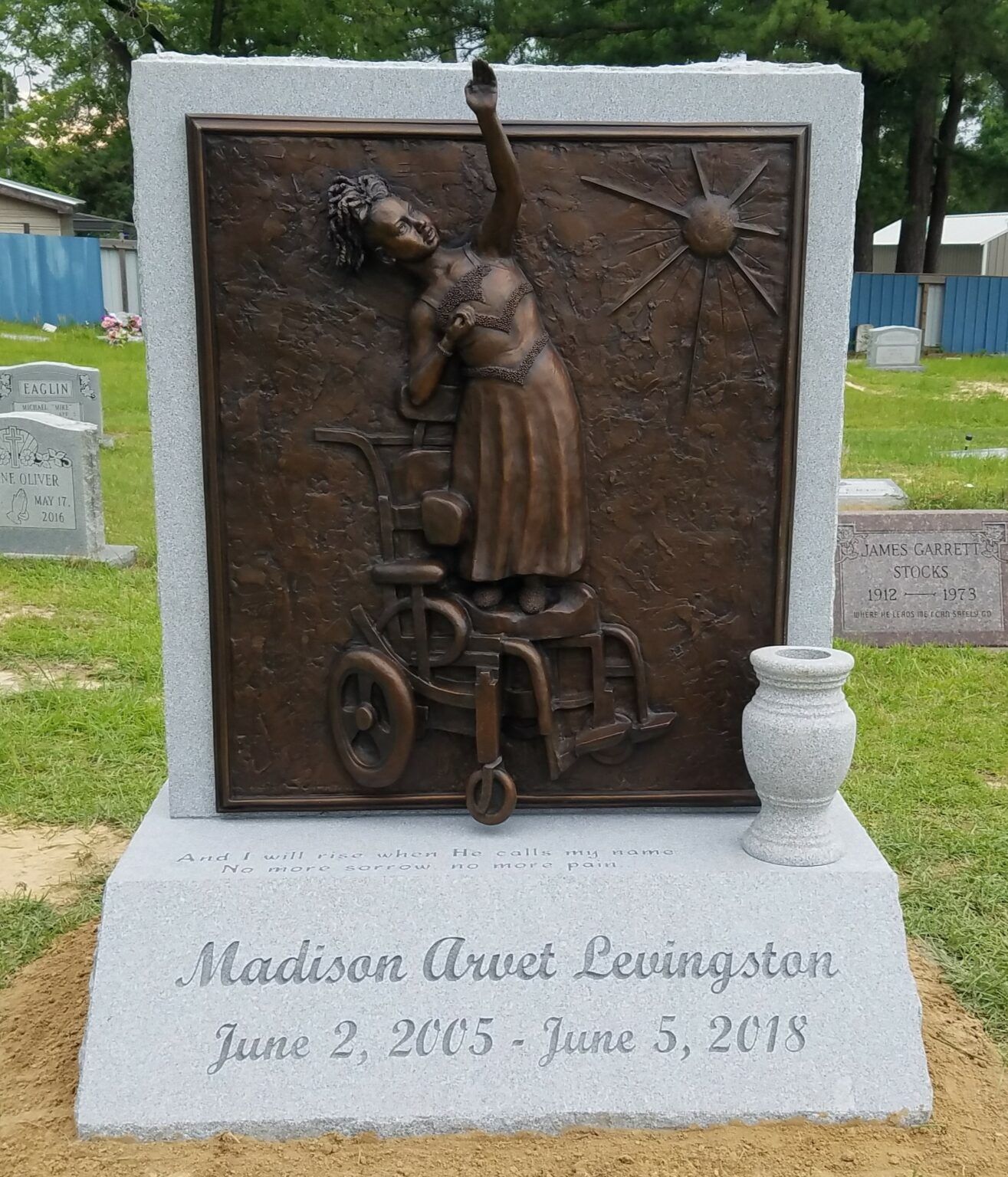 A headstone for Madison Urvet Levingston (2005–2018) featuring a bronze relief of a person rising from a wheelchair.