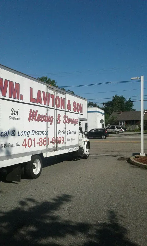 A white Wm. Lawton & Son moving truck turning at an intersection on a sunny day.