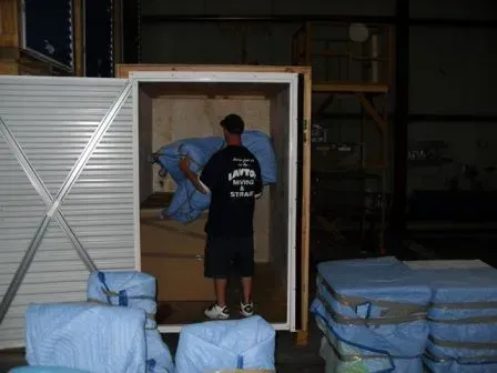 Man carrying wrapped item into storage unit. Inside a warehouse with packed items.