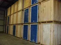 Rows of wooden storage units with blue roll-up doors inside a warehouse.