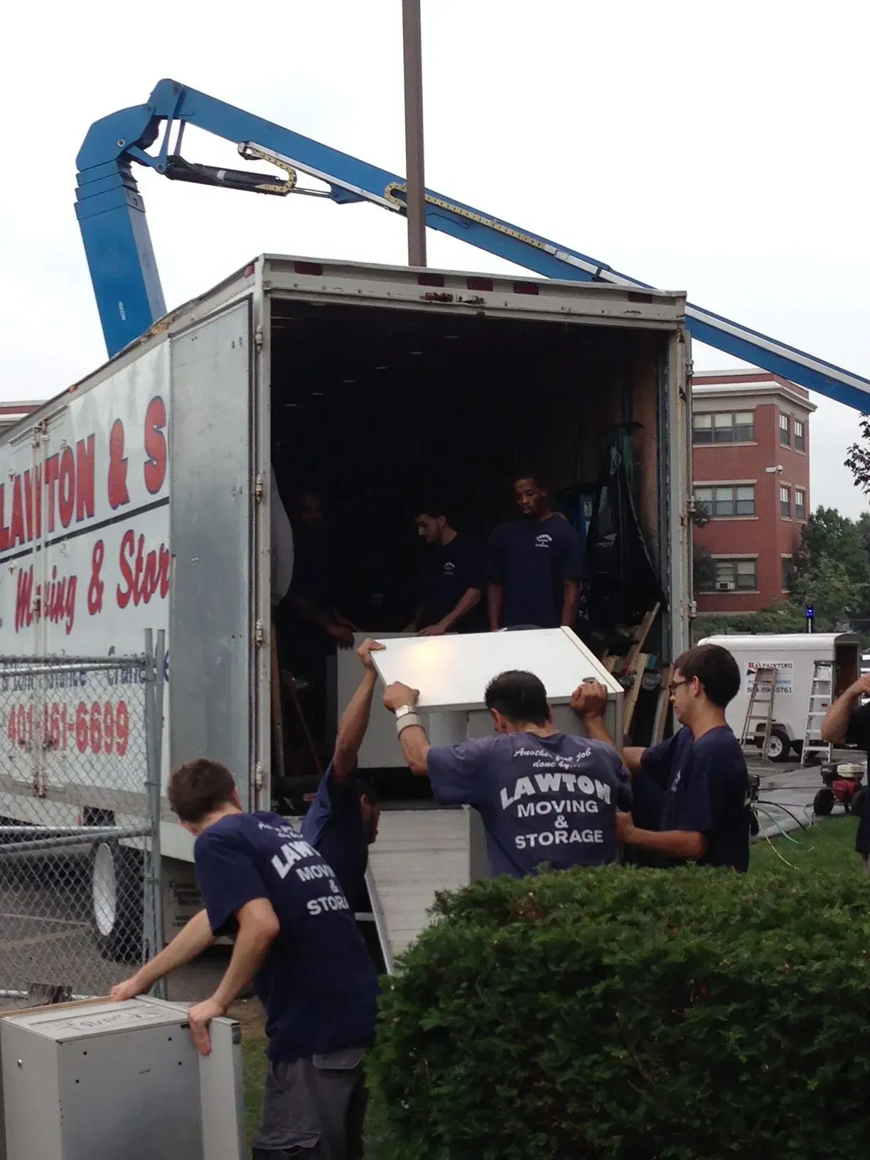 Movers loading a truck with white panels, using a lift outside a building.