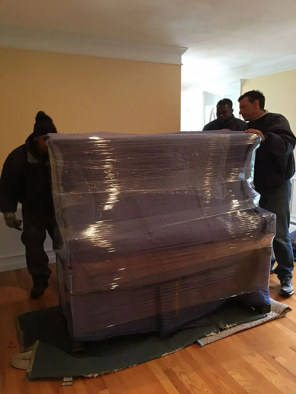 Movers wrapping and moving a piano in a home.