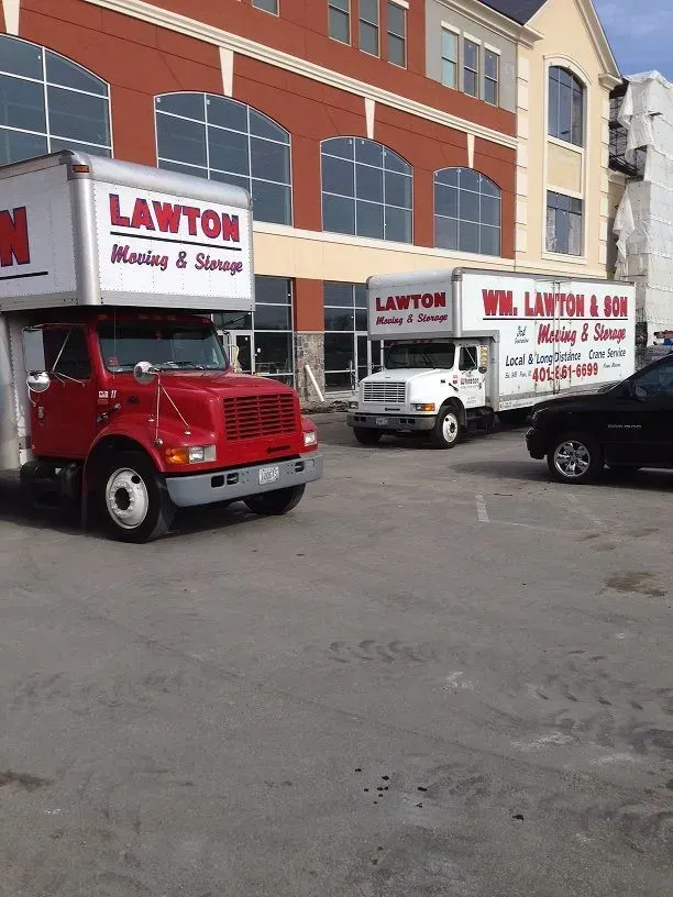 Red and white Lawton Moving & Storage trucks parked in front of a brick building, loading or unloading.
