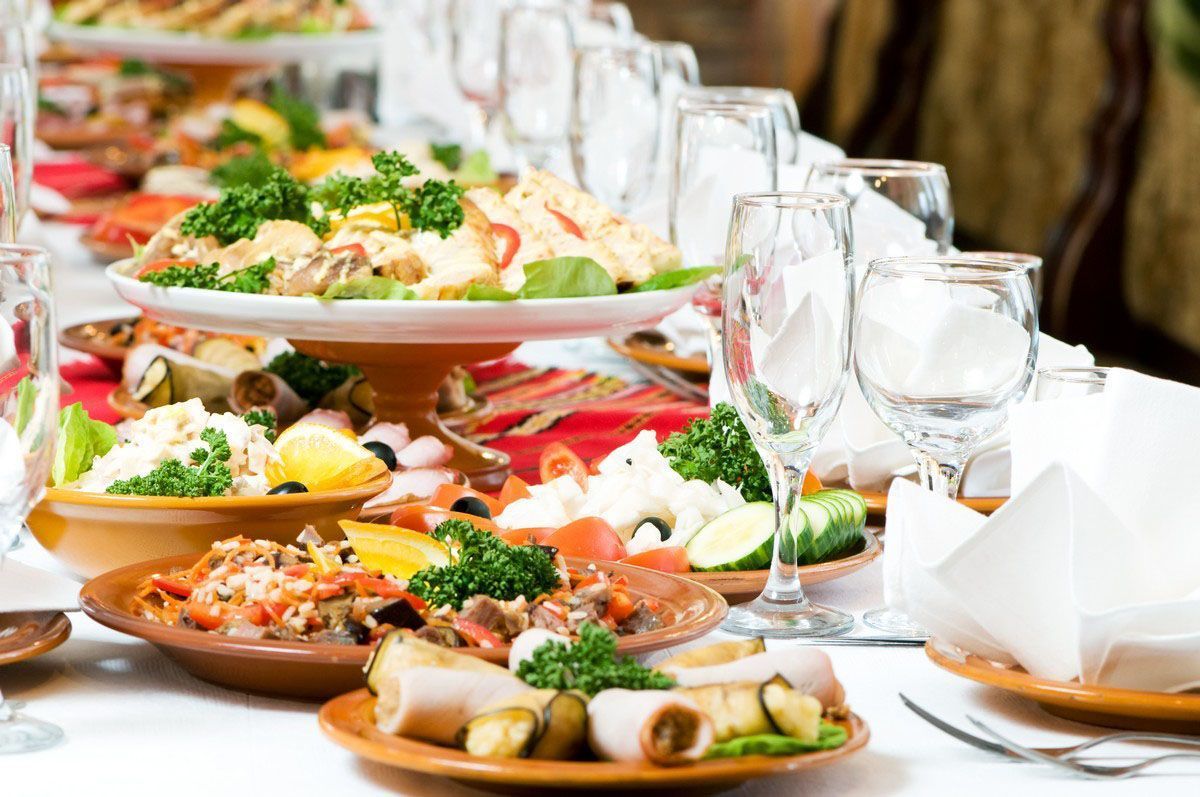 A banquet table set with multiple platters of appetizers, including meats, cheeses, and garnishes, with wine glasses.