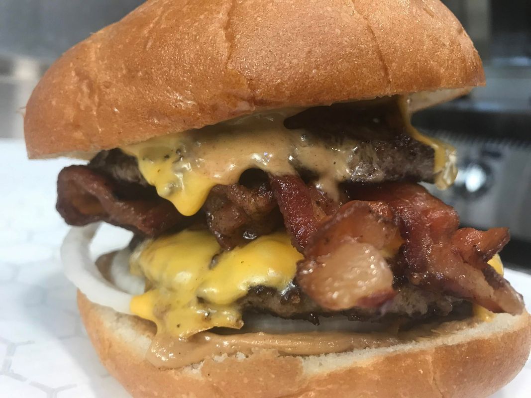 A double cheeseburger with bacon and a slice of raw onion on a toasted bun.