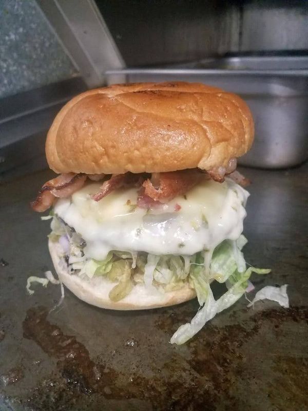 A cheeseburger with bacon and shredded lettuce on a toasted bun, resting on a flat-top grill surface.