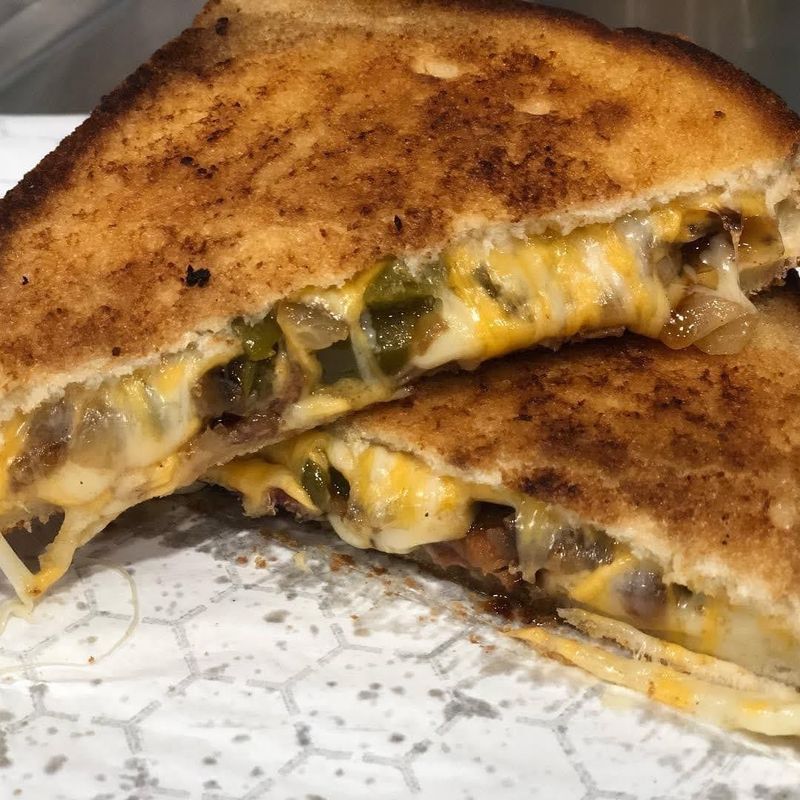 A grilled cheese sandwich sliced in half, featuring melted cheese, green peppers, and onions between toasted bread.
