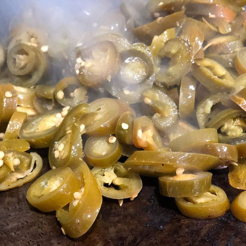 Sautéed, sliced jalapeño peppers with visible seeds steaming on a dark cooking surface.
