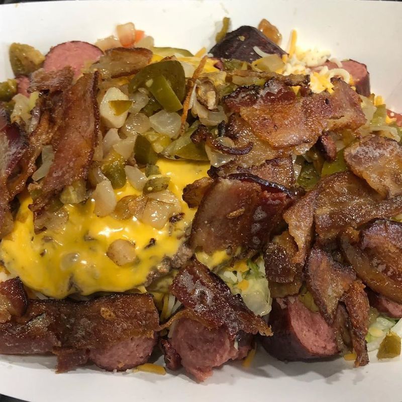 A paper tray filled with chopped sausage, crispy bacon, melted yellow cheese, and diced jalapeños.