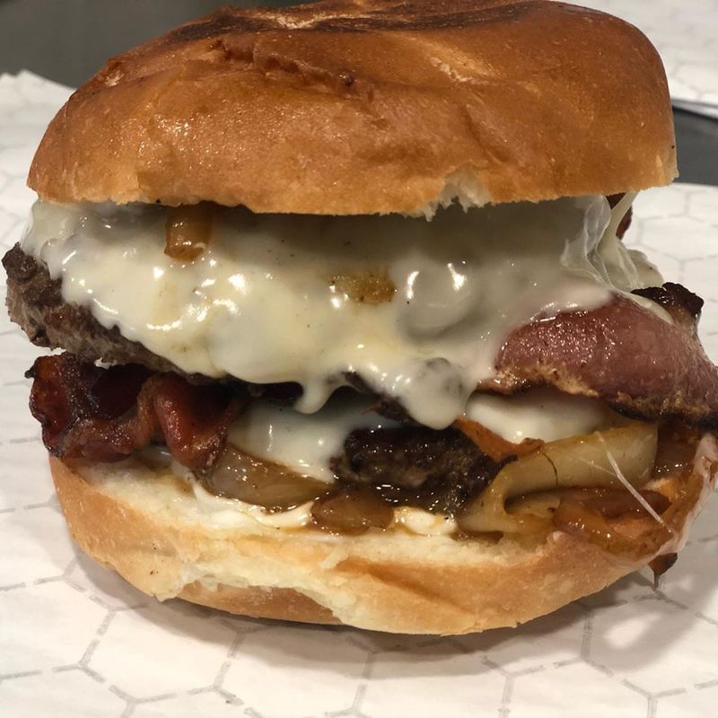 A gourmet cheeseburger on a toasted bun, featuring a beef patty, melted cheese, bacon, and sautéed onions.