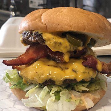 A double cheeseburger with bacon, jalapeños, and lettuce on a soft bun, resting on white paper.