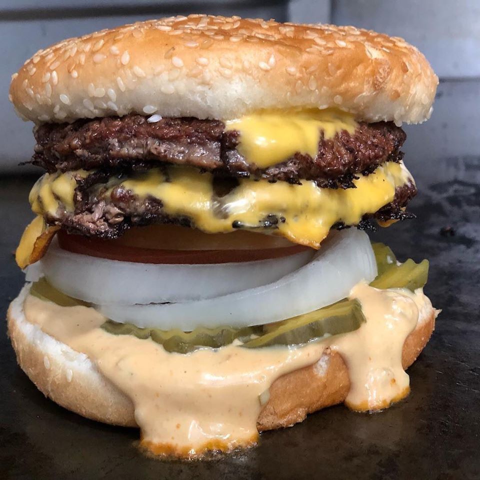 A double cheeseburger on a sesame seed bun with tomato, onion, pickles, and dripping burger sauce.