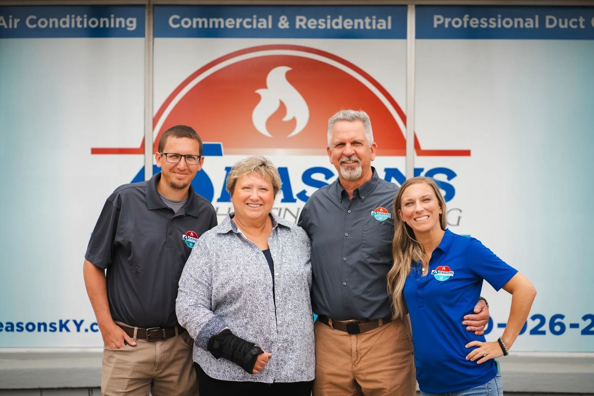Four Seasons Heating & Cooling team in front of their company sign, with a flame logo.