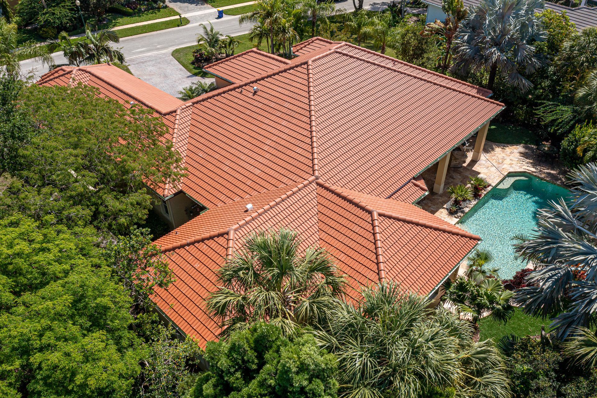 An aerial view of a house with a red tile roof and a pool surrounded by trees.