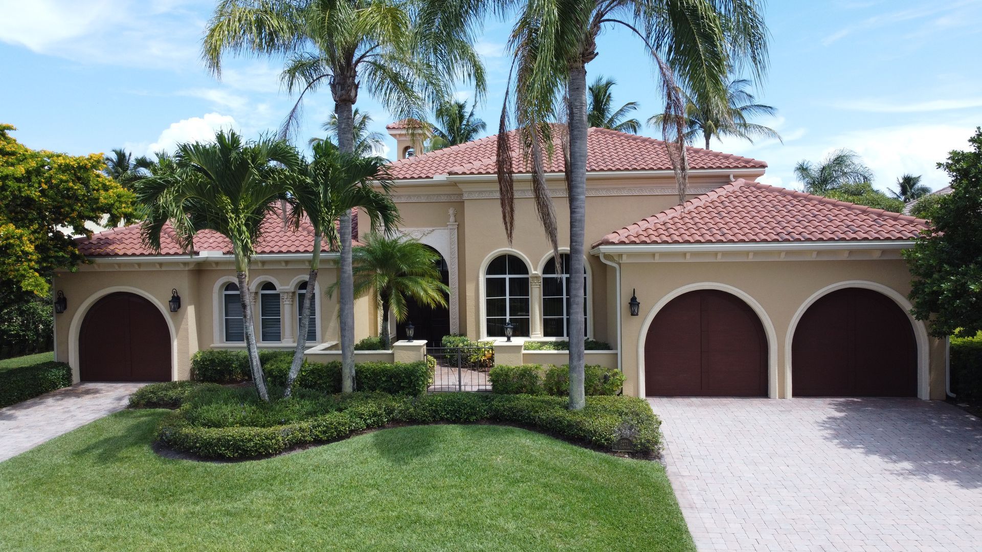A large house with two garages and palm trees in front of it.