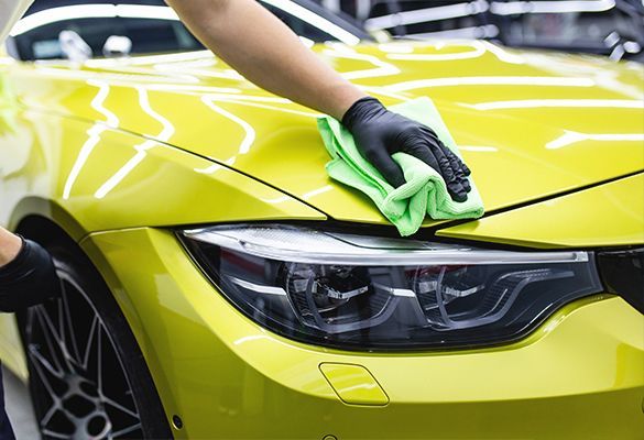 a person is cleaning a yellow car with a cloth