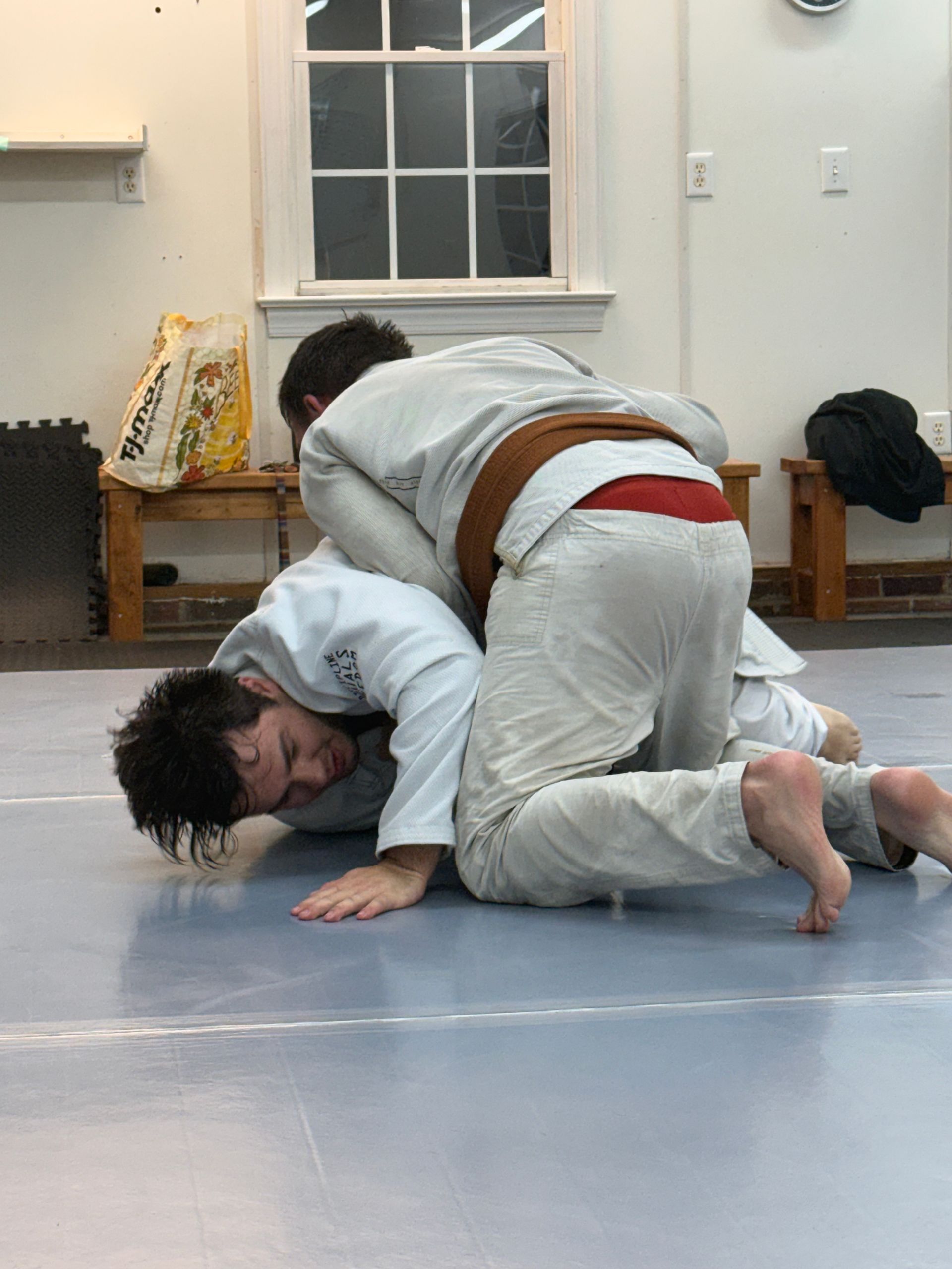Two grapplers in white gis practicing ground control on a mat indoors