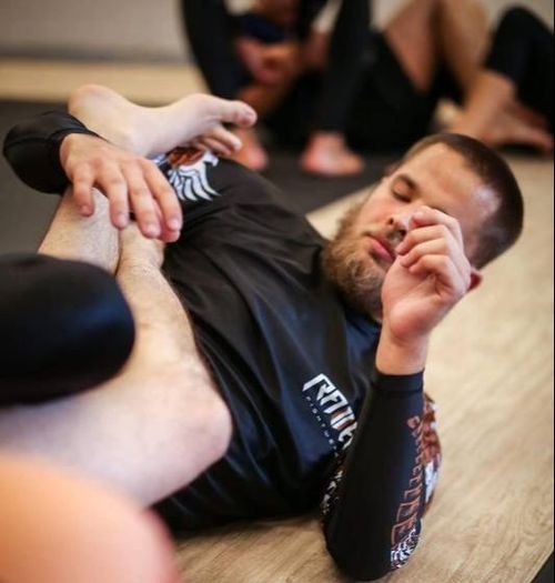 Man practicing Brazilian jiu-jitsu grappling on a mat while a partner holds him in a controlled position