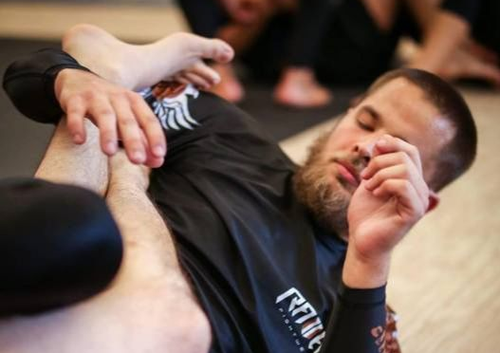 Martial arts training: two people grappling on a mat, one pinning the other with a focused expression