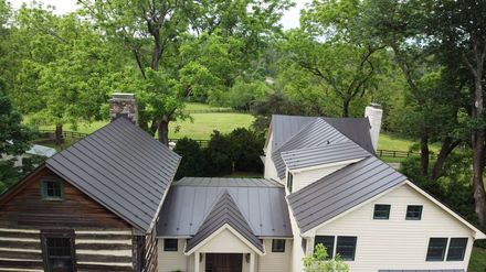 Three connected buildings with dark gray roofs, surrounded by green trees.