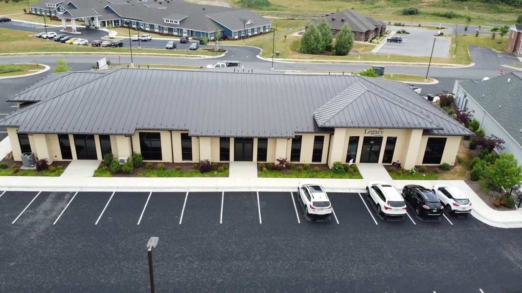 Office building with dark roof, beige walls, and parking lot. Several cars parked in front.