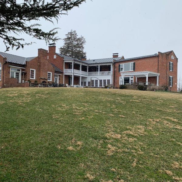 Large brick mansion with multiple levels and a grassy lawn on a cloudy day.