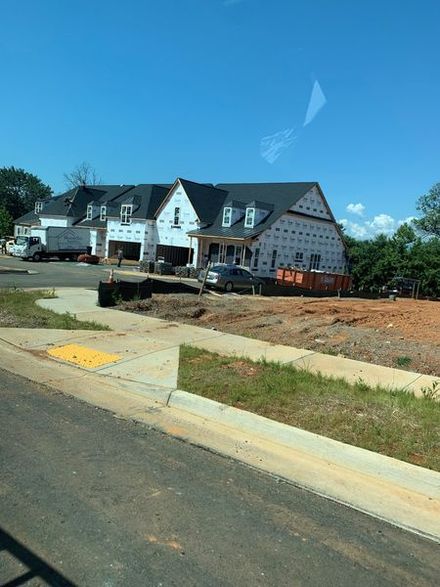 Houses under construction with black roofs, white siding, blue sky.