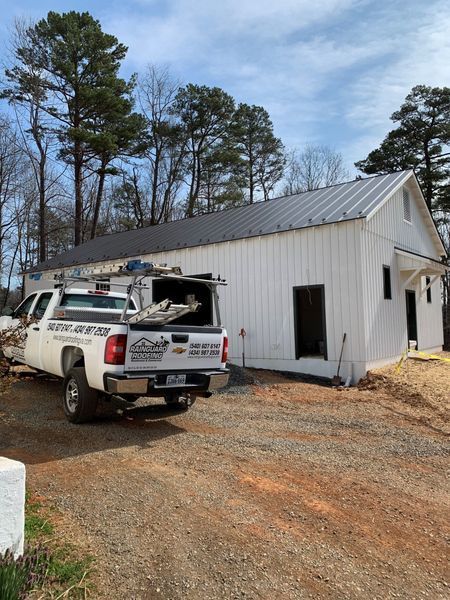 White truck parked next to a white barn-style building with a black roof under a cloudy sky.