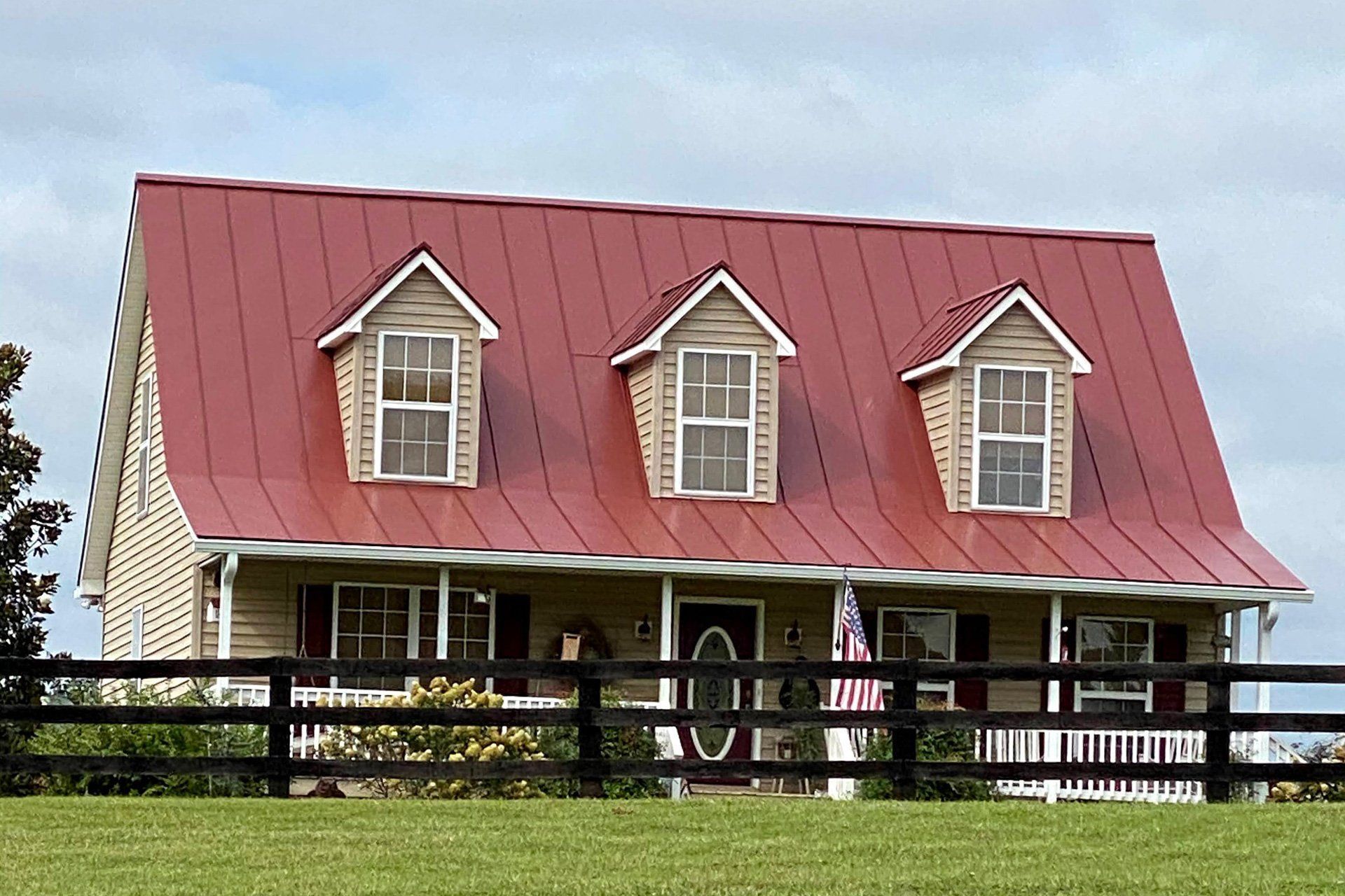 House with a red metal roof and three dormer windows, surrounded by a black fence.