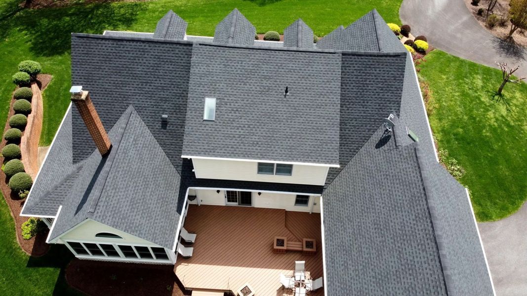 Overhead view of a house with a dark gray shingled roof, a wooden deck, and a green lawn.