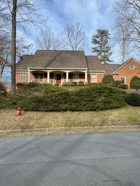 Brick house with a covered porch and red door, surrounded by green bushes and trees.