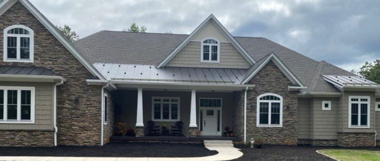 A large suburban home with stone and siding facade, covered porch, and asphalt driveway under an overcast sky.
