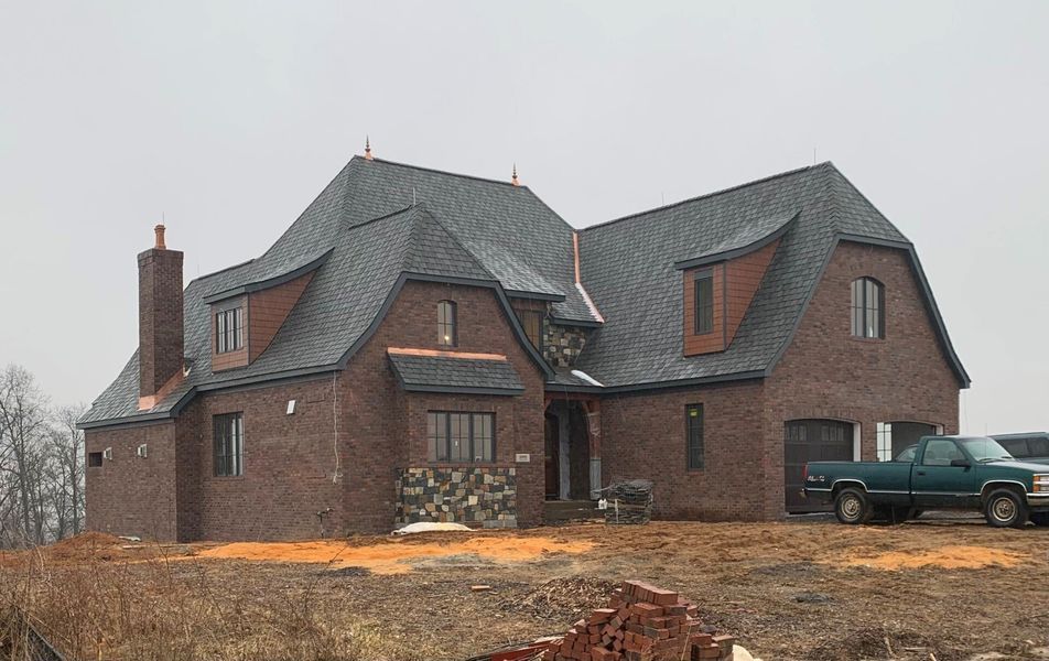 Brick house with dark roof, copper accents, and a green truck parked nearby. Cloudy sky.