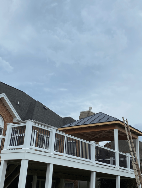 A two-level deck with a gazebo under a cloudy sky, adjacent to a brick house.