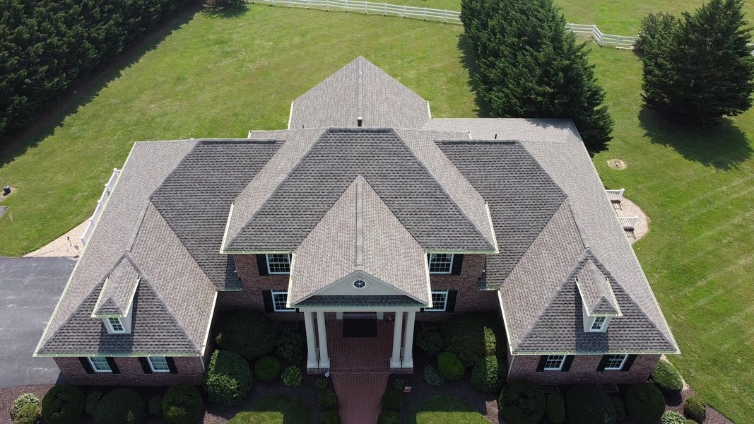 Aerial view of a large house with a multi-gabled roof on a grassy lot.