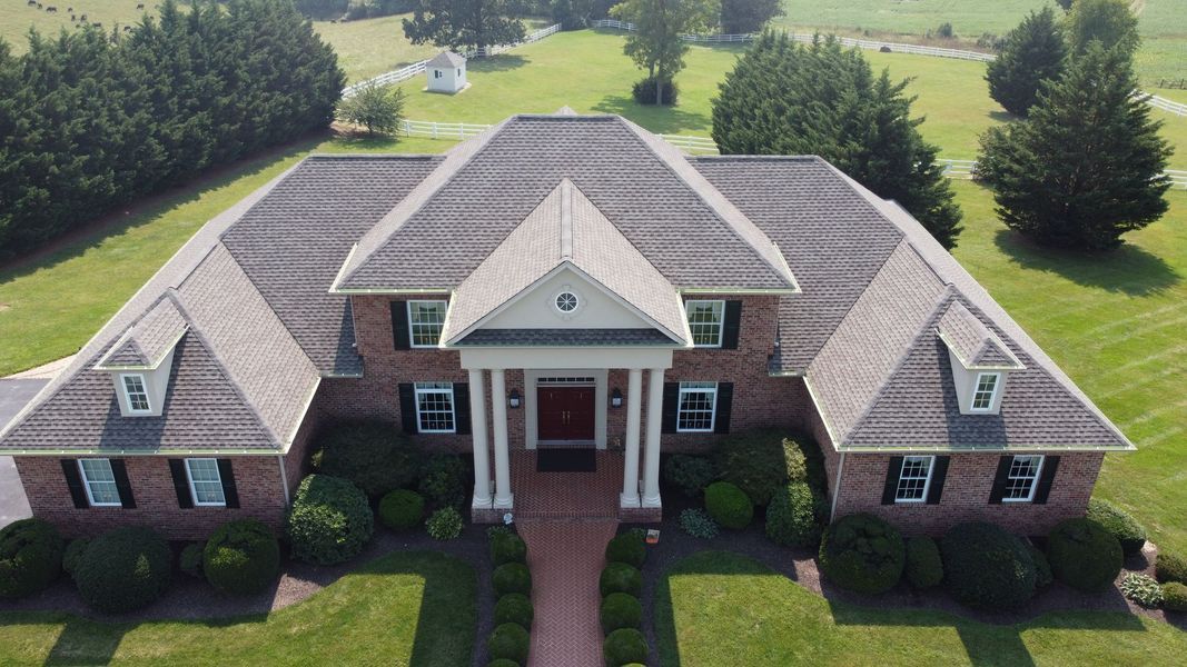 Brick home with gray roof, dormers, and portico on a grassy lot.