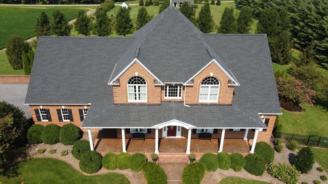 A brick house with a gray roof, two-story with a porch and green landscaping.