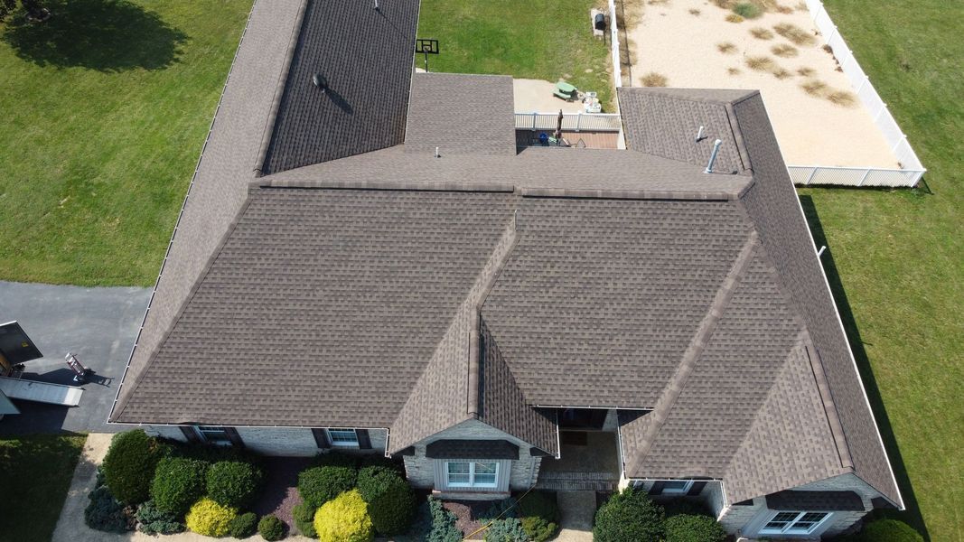 Aerial view of a brown-roofed house with green lawn, bushes, and a pathway to the entrance.