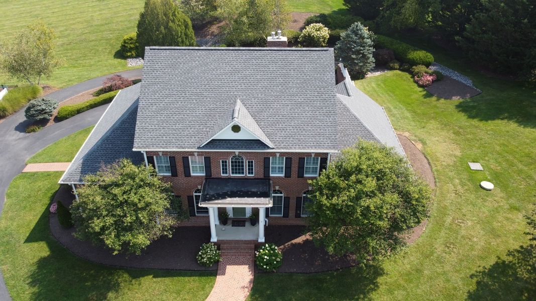 Aerial view of a two-story brick house with a gray roof and landscaping, surrounded by green grass.
