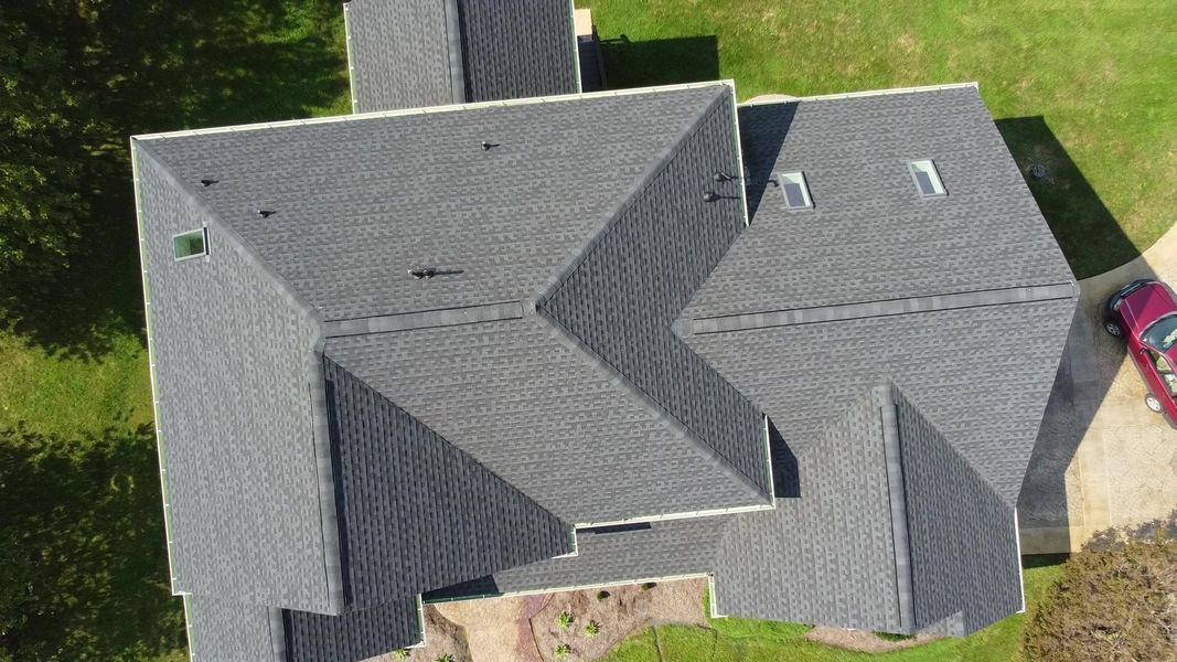 Overhead view of a house with a gray shingle roof, green grass, and a red car parked nearby.
