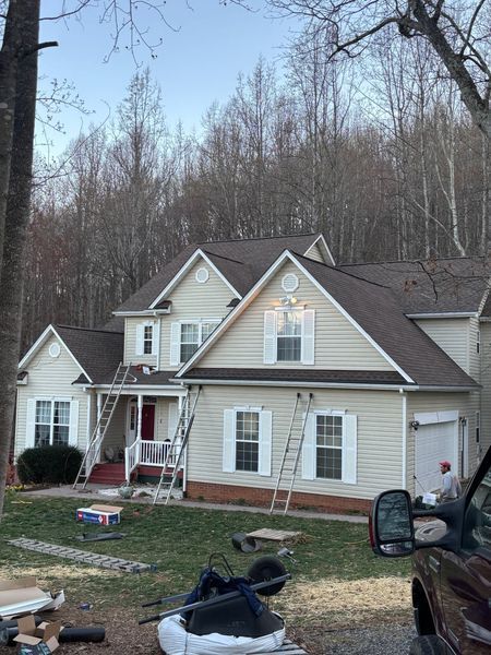 Beige house with brown roof and white shutters. Ladders propped on side.