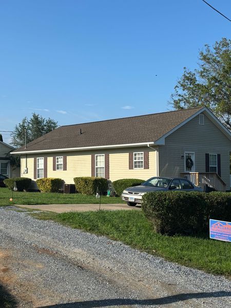 Tan house with brown trim and roof, shrubs, car in driveway.