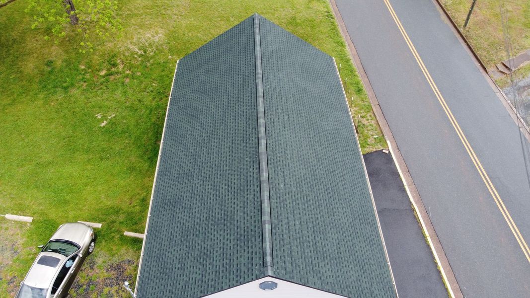 Overhead view of a building with a dark green shingled roof next to a road and grassy area.