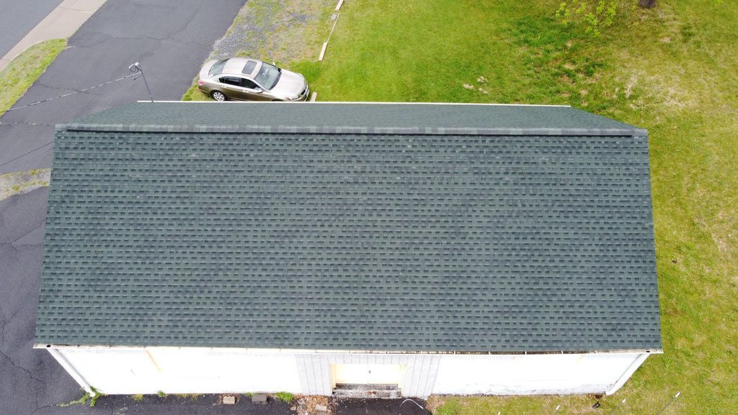 Overhead view of a white building with a green shingled roof, a car, and green grass.