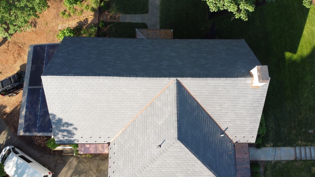 Overhead view of a house roof with a chimney, trees, and a pathway visible.