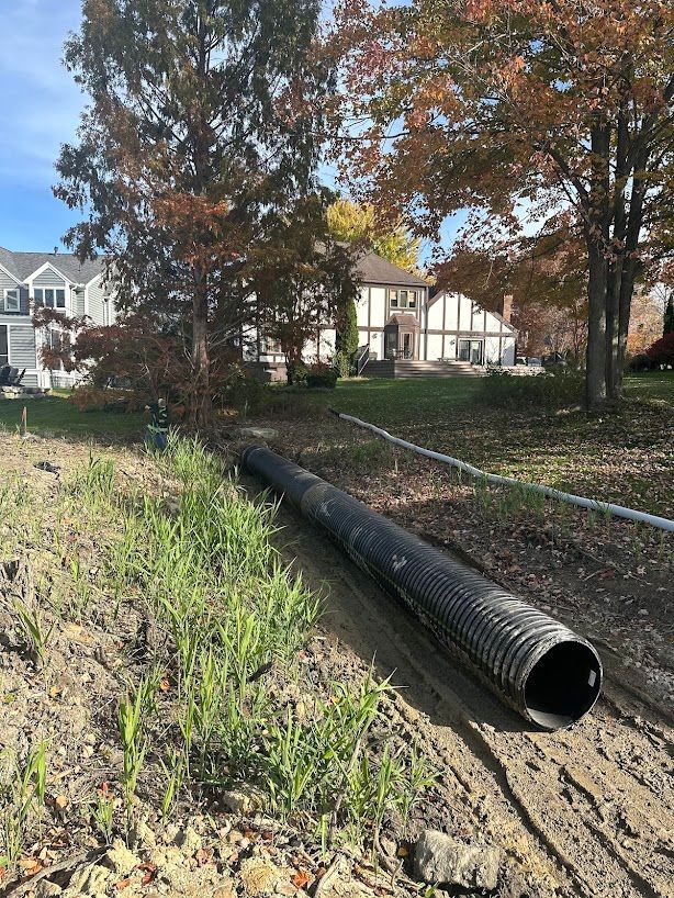 A large black pipe is laying in the dirt in front of a house.