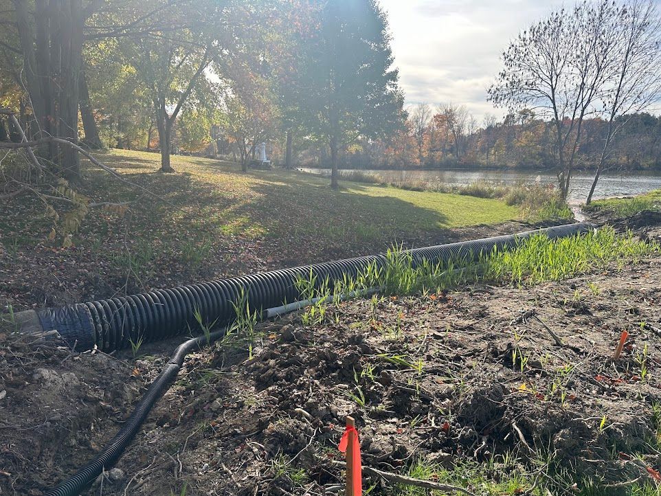 A large pipe is sitting in the middle of a field next to a river.