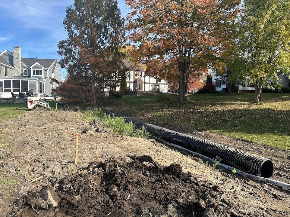 A large pipe is being installed in a dirt field in front of a house.