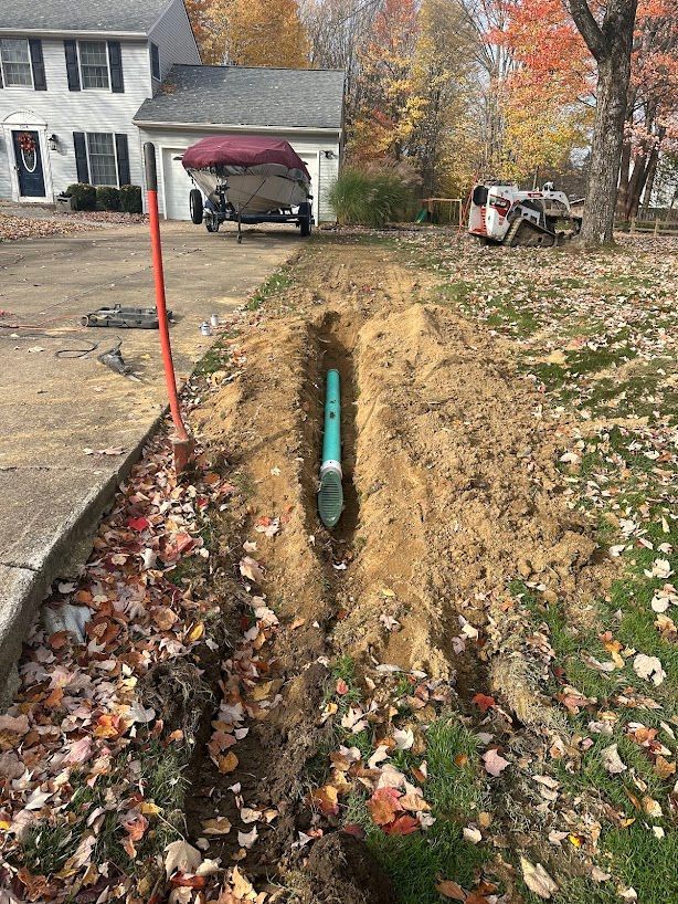 A drain pipe is being installed in the dirt in front of a house.