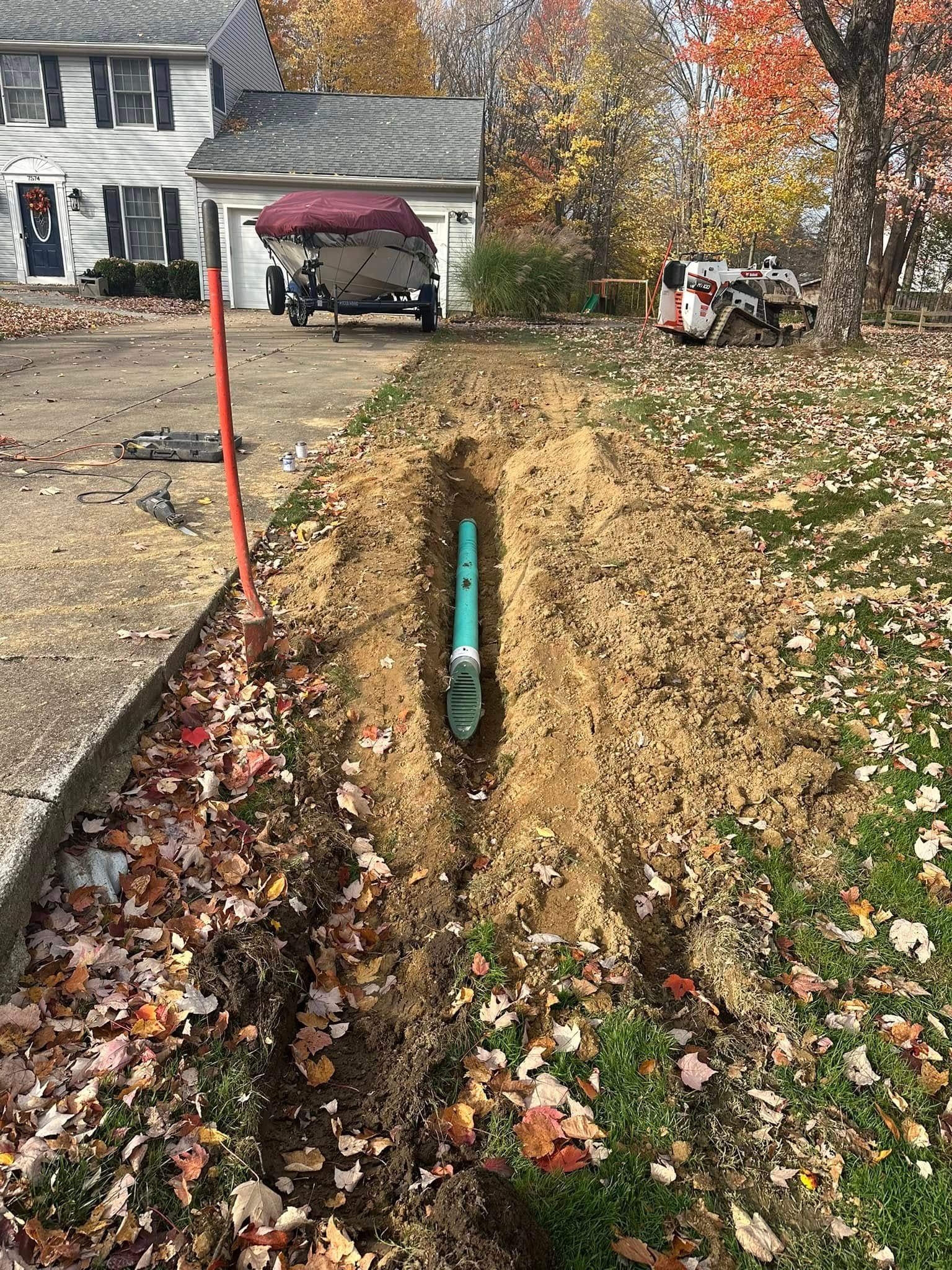 A green pipe is being installed in the dirt in front of a house.